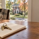 House keys on a folder of deed paperwork on a kitchen table, with a brick home outside the window